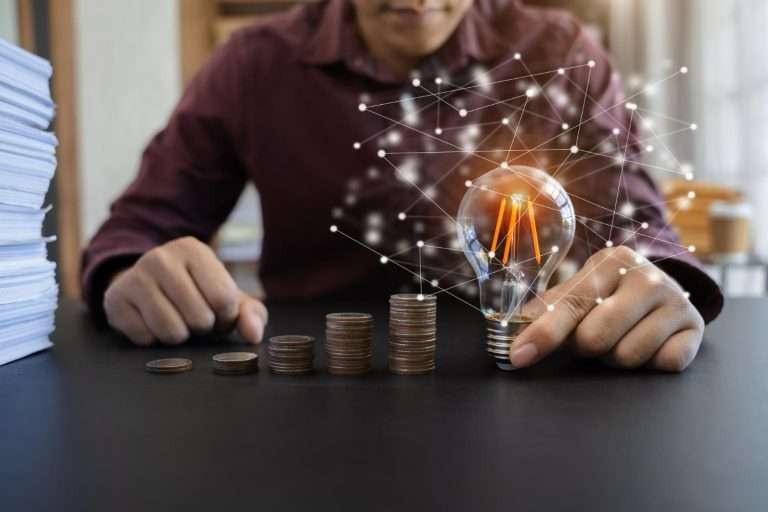 business men hand holding lightbulb with coins stack desk concept saving energy money office